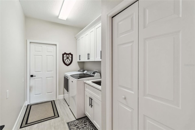 laundry room featuring cabinets, separate washer and dryer, a textured ceiling, and light hardwood / wood-style flooring