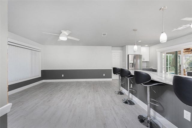 interior space featuring light hardwood / wood-style flooring, white cabinetry, a kitchen breakfast bar, stainless steel refrigerator with ice dispenser, and decorative light fixtures