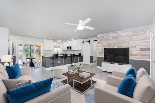 living room with ceiling fan, a barn door, sink, and light hardwood / wood-style flooring