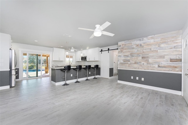 kitchen with appliances with stainless steel finishes, kitchen peninsula, ceiling fan, a barn door, and white cabinets