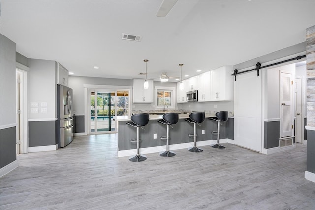 kitchen with pendant lighting, white cabinets, kitchen peninsula, stainless steel appliances, and a barn door