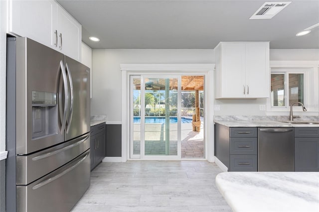 kitchen with appliances with stainless steel finishes, white cabinetry, sink, gray cabinetry, and light stone counters