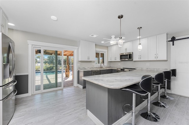 kitchen featuring appliances with stainless steel finishes, white cabinets, a kitchen bar, hanging light fixtures, and kitchen peninsula