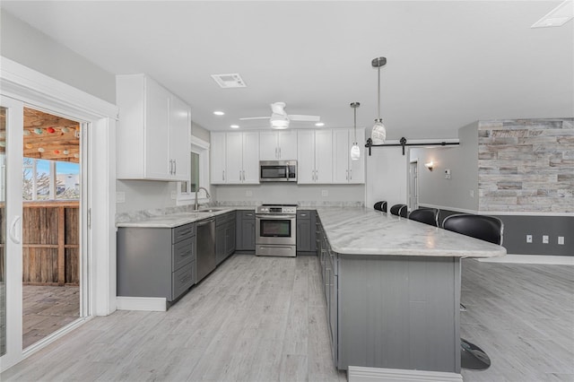 kitchen with appliances with stainless steel finishes, decorative light fixtures, a breakfast bar area, gray cabinetry, and a barn door