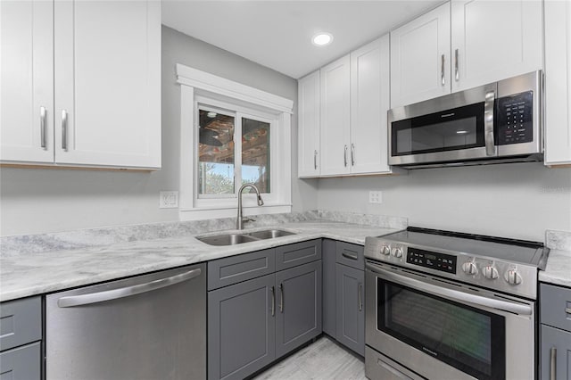 kitchen with sink, gray cabinets, appliances with stainless steel finishes, light stone counters, and white cabinets