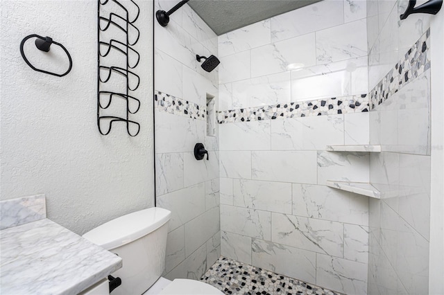 bathroom featuring vanity, a tile shower, and toilet