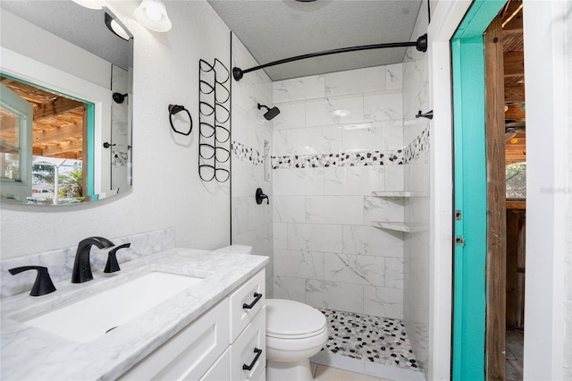 bathroom with vanity, toilet, a textured ceiling, and a tile shower