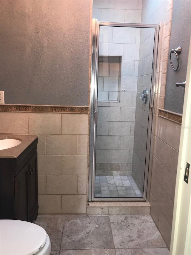 bathroom featuring a shower with door, vanity, tile walls, and toilet