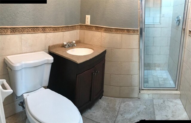 bathroom with vanity, a shower with shower door, tile walls, and toilet