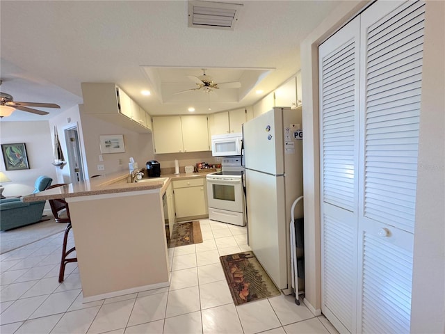 kitchen featuring a breakfast bar, ceiling fan, kitchen peninsula, a raised ceiling, and white appliances