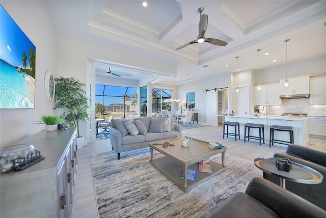 living room with beamed ceiling, a barn door, coffered ceiling, and ceiling fan