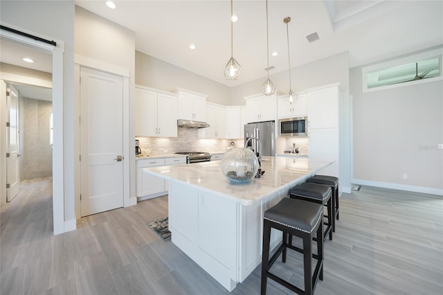 kitchen featuring white cabinetry, hanging light fixtures, a center island with sink, stainless steel appliances, and a kitchen bar