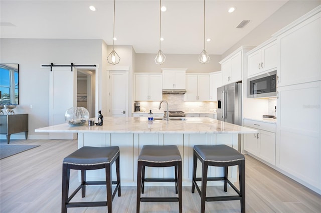 kitchen featuring black microwave, high quality fridge, a barn door, a kitchen island with sink, and white cabinets