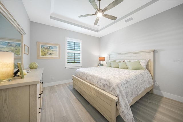 bedroom with light hardwood / wood-style floors, a raised ceiling, and ceiling fan