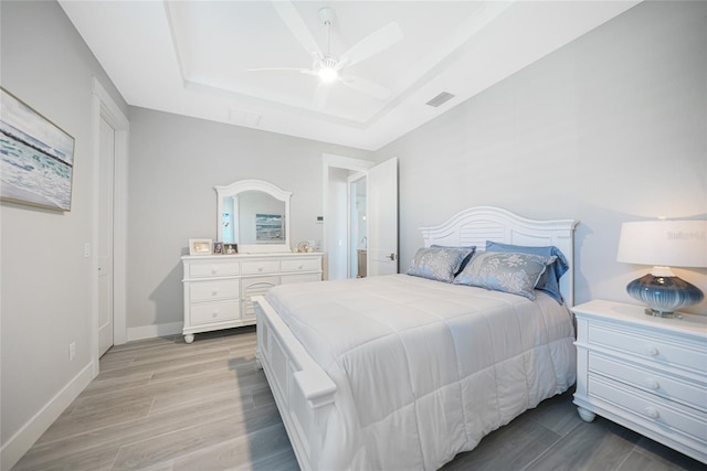 bedroom with a raised ceiling, ceiling fan, and light hardwood / wood-style floors