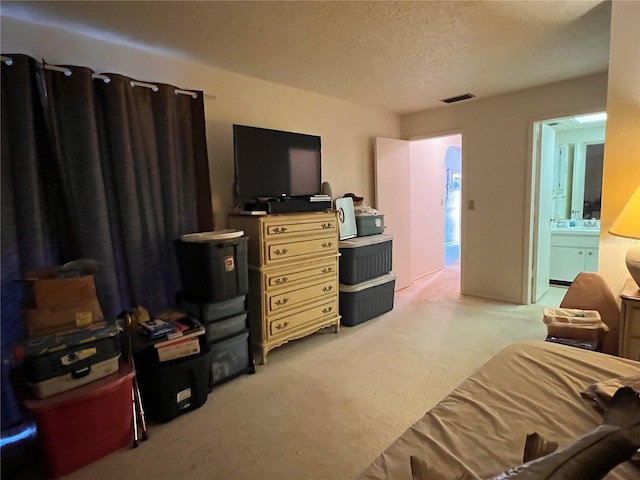 bedroom with light colored carpet, a textured ceiling, and ensuite bathroom