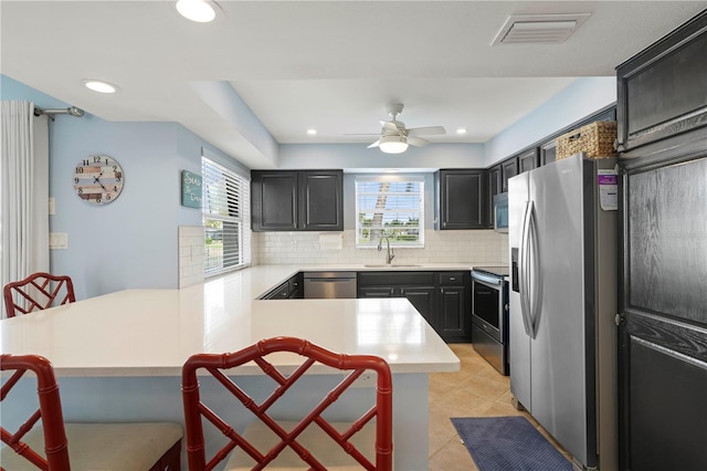 kitchen with light tile patterned flooring, appliances with stainless steel finishes, sink, backsplash, and kitchen peninsula