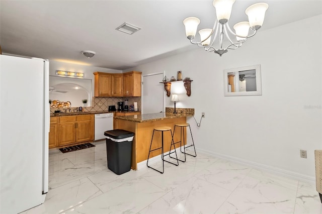 kitchen featuring a breakfast bar, decorative light fixtures, kitchen peninsula, white appliances, and decorative backsplash