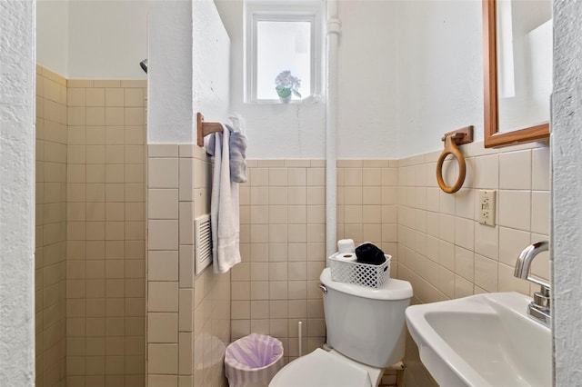 bathroom with toilet, sink, and tile walls