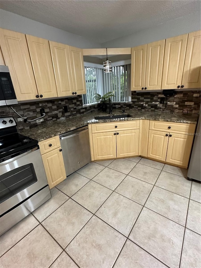 kitchen with sink, light tile patterned floors, appliances with stainless steel finishes, pendant lighting, and dark stone counters