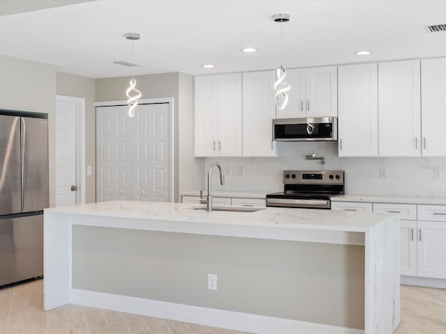 kitchen with sink, a kitchen island with sink, hanging light fixtures, stainless steel appliances, and white cabinets