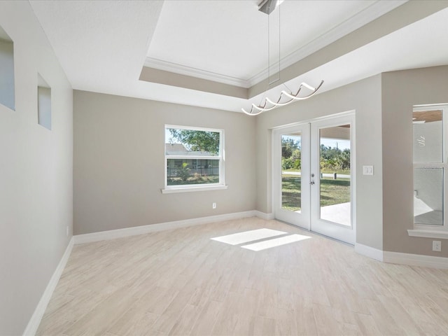 spare room with a tray ceiling, light hardwood / wood-style flooring, ornamental molding, and french doors