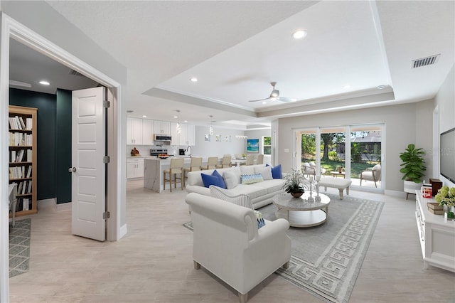 living room featuring ceiling fan, light wood-type flooring, and a tray ceiling