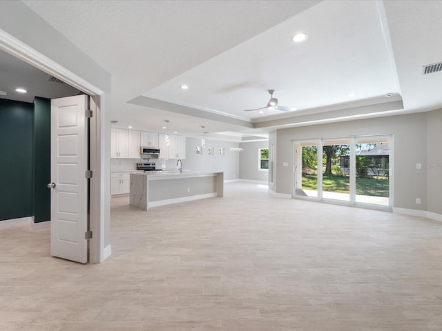 unfurnished living room with sink, light hardwood / wood-style floors, a raised ceiling, and ceiling fan