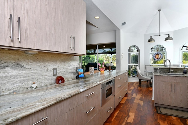 kitchen featuring sink, decorative light fixtures, stainless steel microwave, light stone countertops, and backsplash