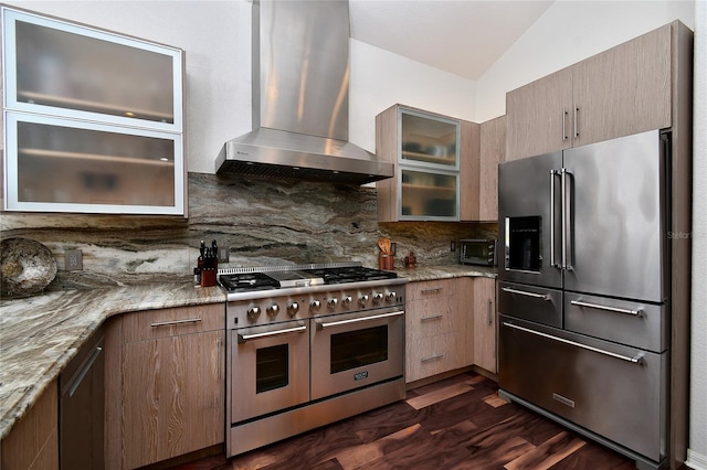 kitchen featuring vaulted ceiling, tasteful backsplash, premium appliances, light stone counters, and wall chimney range hood