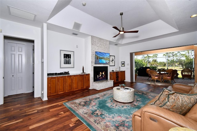 living room with dark hardwood / wood-style flooring, a fireplace, a raised ceiling, and ceiling fan