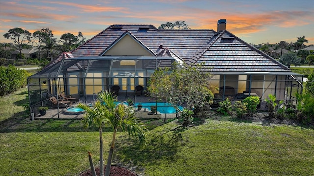 back house at dusk with a patio, a lanai, and a lawn