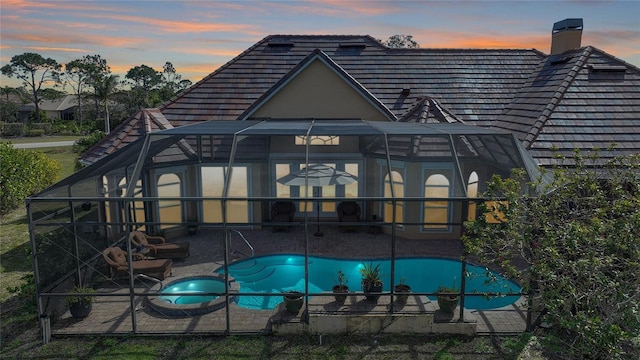 back house at dusk with a patio and glass enclosure