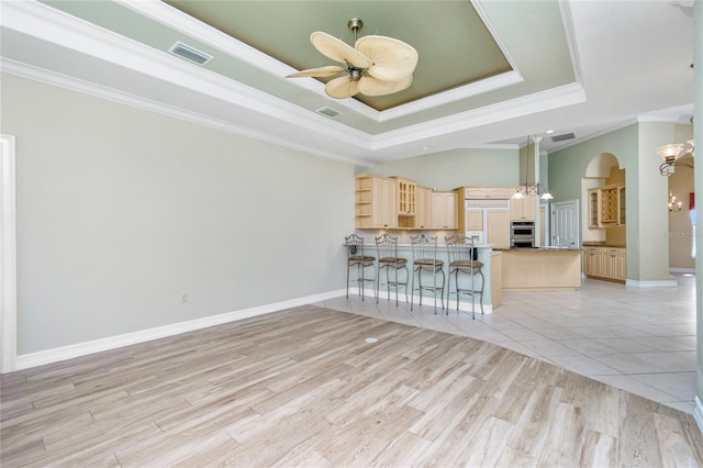 unfurnished living room featuring ceiling fan with notable chandelier, a tray ceiling, arched walkways, and visible vents