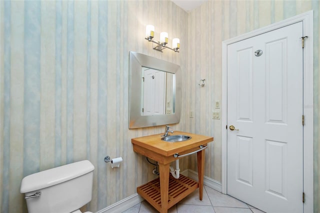 half bath with tile patterned floors, toilet, a sink, wallpapered walls, and baseboards