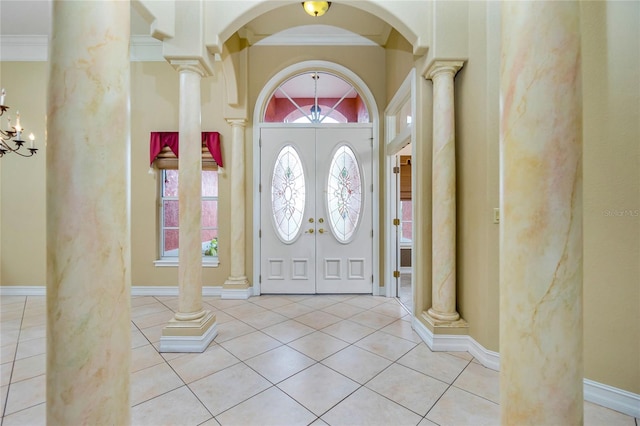 tiled entryway featuring baseboards, ornamental molding, an inviting chandelier, arched walkways, and ornate columns