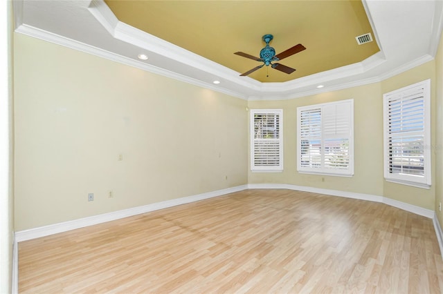 empty room featuring light wood-style floors, a raised ceiling, a ceiling fan, and ornamental molding