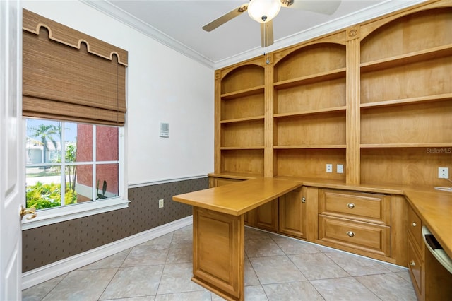 unfurnished office featuring light tile patterned flooring, ceiling fan, built in desk, wainscoting, and crown molding