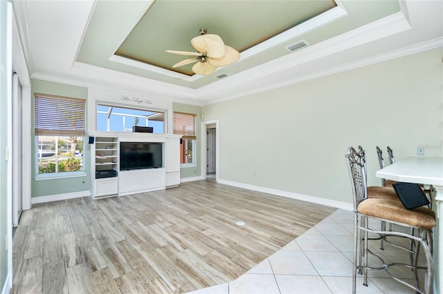 unfurnished living room with a tray ceiling, visible vents, ornamental molding, and a ceiling fan