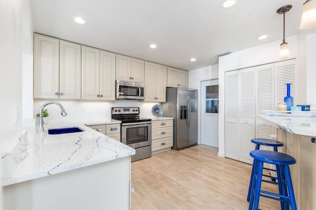 kitchen featuring decorative light fixtures, sink, stainless steel appliances, light stone countertops, and light wood-type flooring