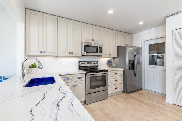 kitchen with stainless steel appliances, light stone countertops, sink, and light wood-type flooring