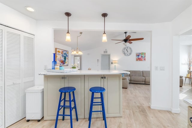 kitchen featuring a breakfast bar, lofted ceiling, hanging light fixtures, ceiling fan, and light hardwood / wood-style flooring