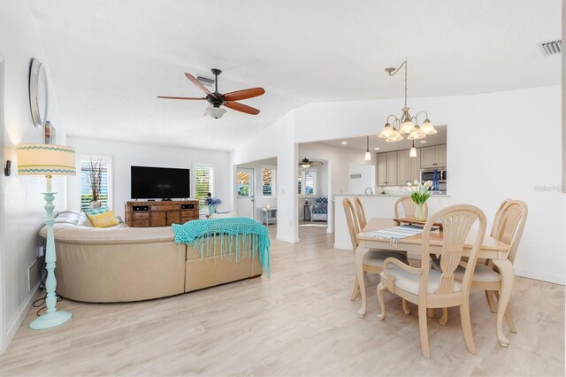 living room with ceiling fan with notable chandelier, vaulted ceiling, and light hardwood / wood-style floors