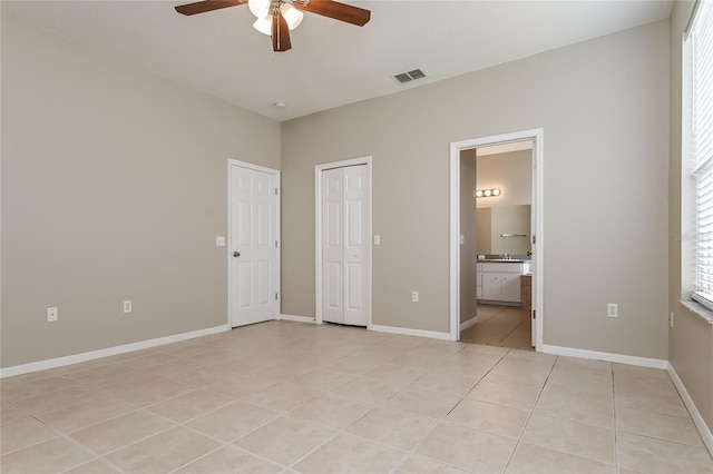 unfurnished bedroom with connected bathroom, light tile patterned floors, and ceiling fan