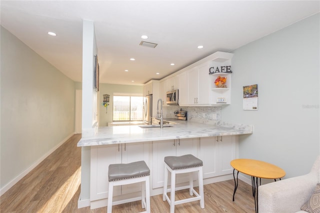 kitchen with a breakfast bar, white cabinetry, light wood-type flooring, appliances with stainless steel finishes, and kitchen peninsula