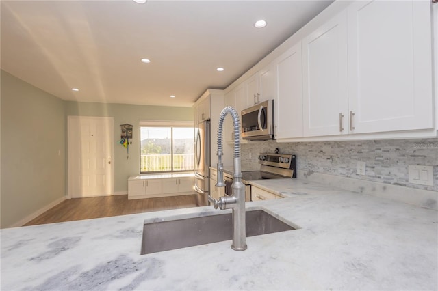 kitchen with appliances with stainless steel finishes, white cabinetry, wood-type flooring, sink, and light stone countertops