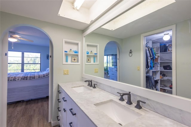 bathroom with built in features, a skylight, wood-type flooring, vanity, and ceiling fan