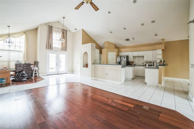 unfurnished living room featuring ceiling fan with notable chandelier, light hardwood / wood-style flooring, and high vaulted ceiling