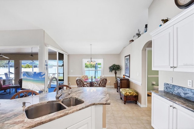 kitchen with vaulted ceiling, pendant lighting, sink, white cabinets, and dark stone counters