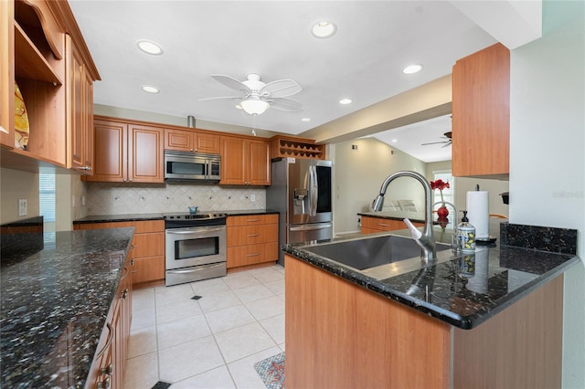 kitchen featuring appliances with stainless steel finishes, sink, dark stone counters, light tile patterned floors, and ceiling fan